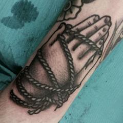 Praying hands bound by rope